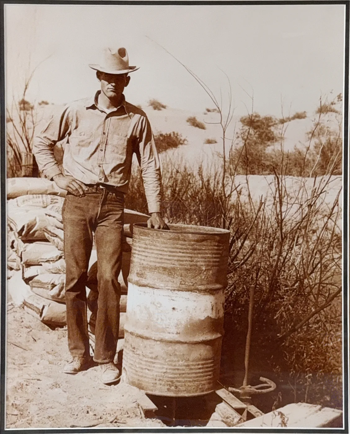 A young Barkley farmer stands beside an oil drum among the sand dunes of the early Yuma Valley